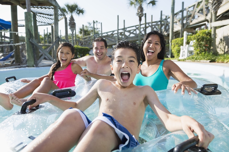 Multi-ethnic family with two children having fun at water park. Main focus on boy (9 years).